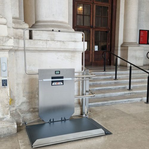 GTLE Plattform-Treppenlift mit gebogener Führungsschiene entlang einer Marmortreppe vor einem Gebäude mit klassischer Fassade – barrierefreie Zugangslösung für Rollstuhlfahrer oder Personen mit eingeschränkter Mobilität, integriert in ein historisch anmutendes architektonisches Umfeld.