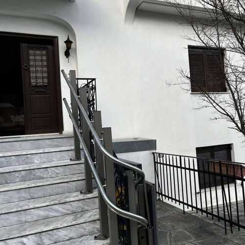 GTLE Plattform-Treppenlift mit gebogener Führungsschiene entlang einer Marmortreppe am Eingang eines Gebäudes mit weißer Fassade – barrierefreie Zugangslösung für Rollstuhlfahrer oder Personen mit eingeschränkter Mobilität im öffentlichen oder privaten Bereich.