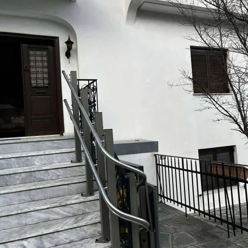 GTLE Plattform-Treppenlift mit gebogener Führungsschiene entlang einer Marmortreppe am Eingang eines Gebäudes mit weißer Fassade – barrierefreie Zugangslösung für Rollstuhlfahrer oder Personen mit eingeschränkter Mobilität im öffentlichen oder privaten Bereich.