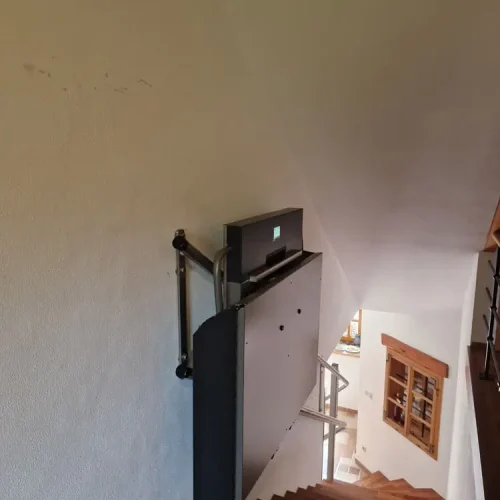 GTLE Plattform-Treppenlift im zusammengeklappten Zustand, montiert an einer Holztreppe im Innenbereich eines Wohnhauses – platzsparende und barrierefreie Lösung für Personen mit eingeschränkter Mobilität zur sicheren Überwindung von Treppen.